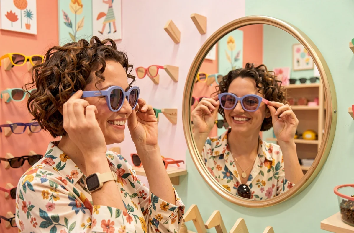 Jeune femme essayant des lunettes colorées dans la boutique Loulou au décor joyeux et créatif